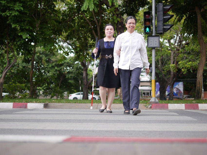 A person is guiding a person with a visual impairment across a road.